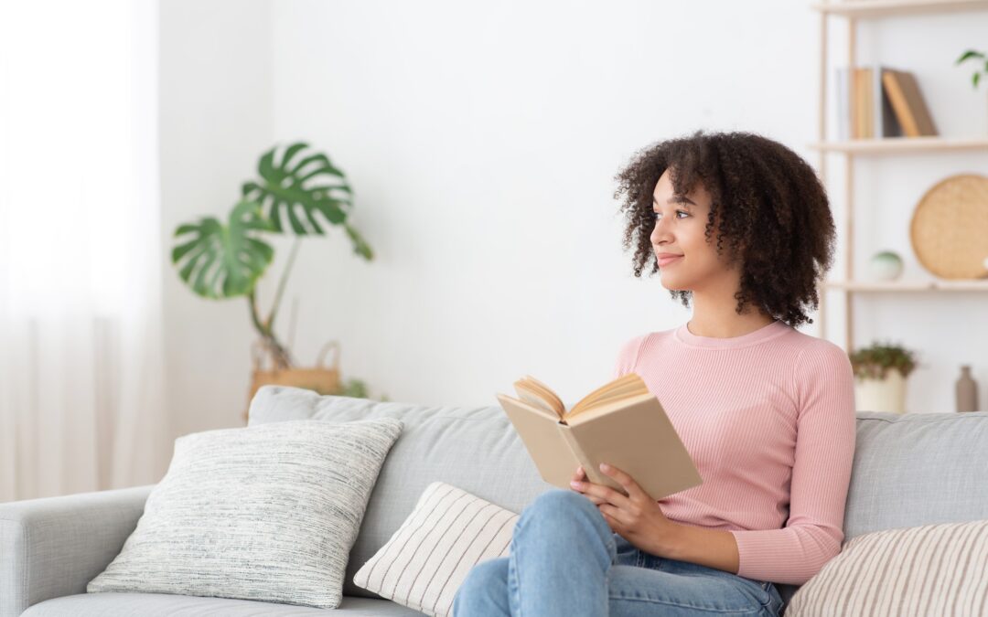 A black woman sits on a sofa with a book breathing in fresh air from her air purification system.